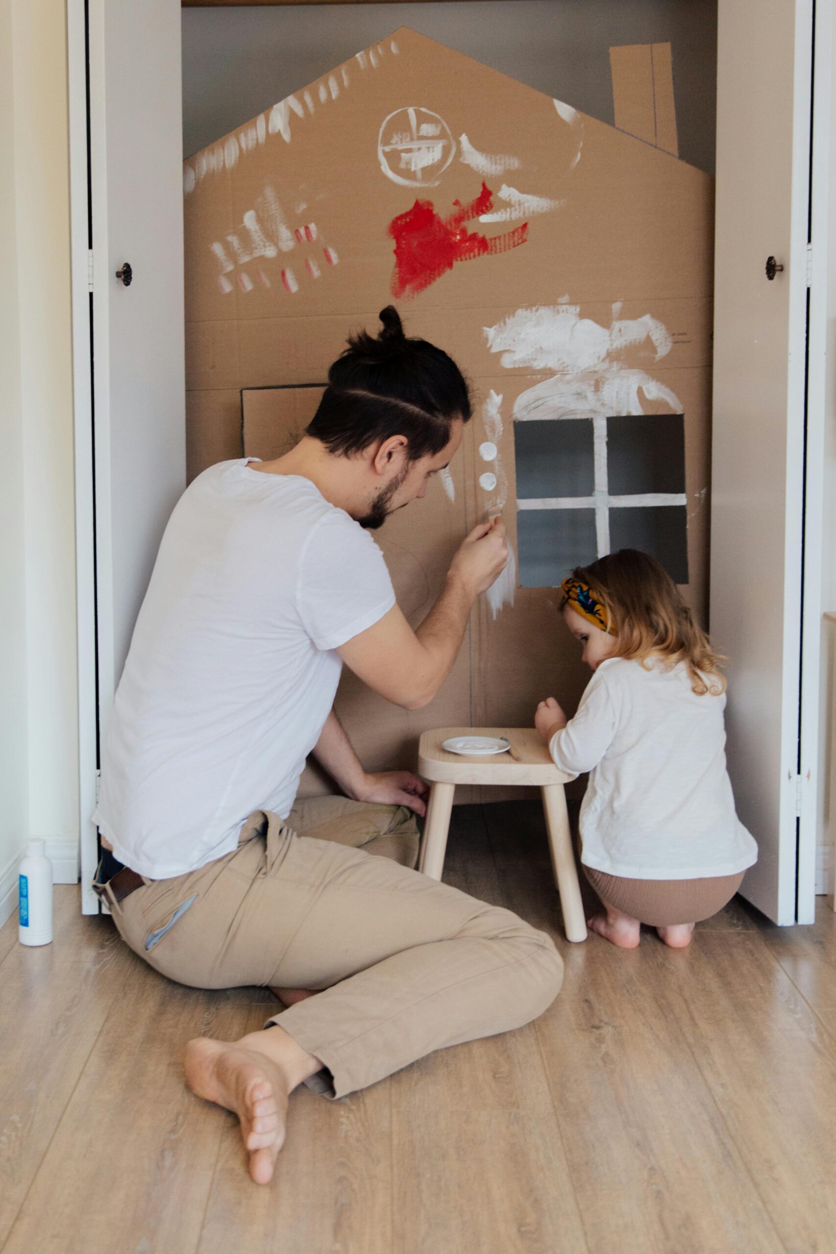 Father plays with daughter in her painted cardboard house.