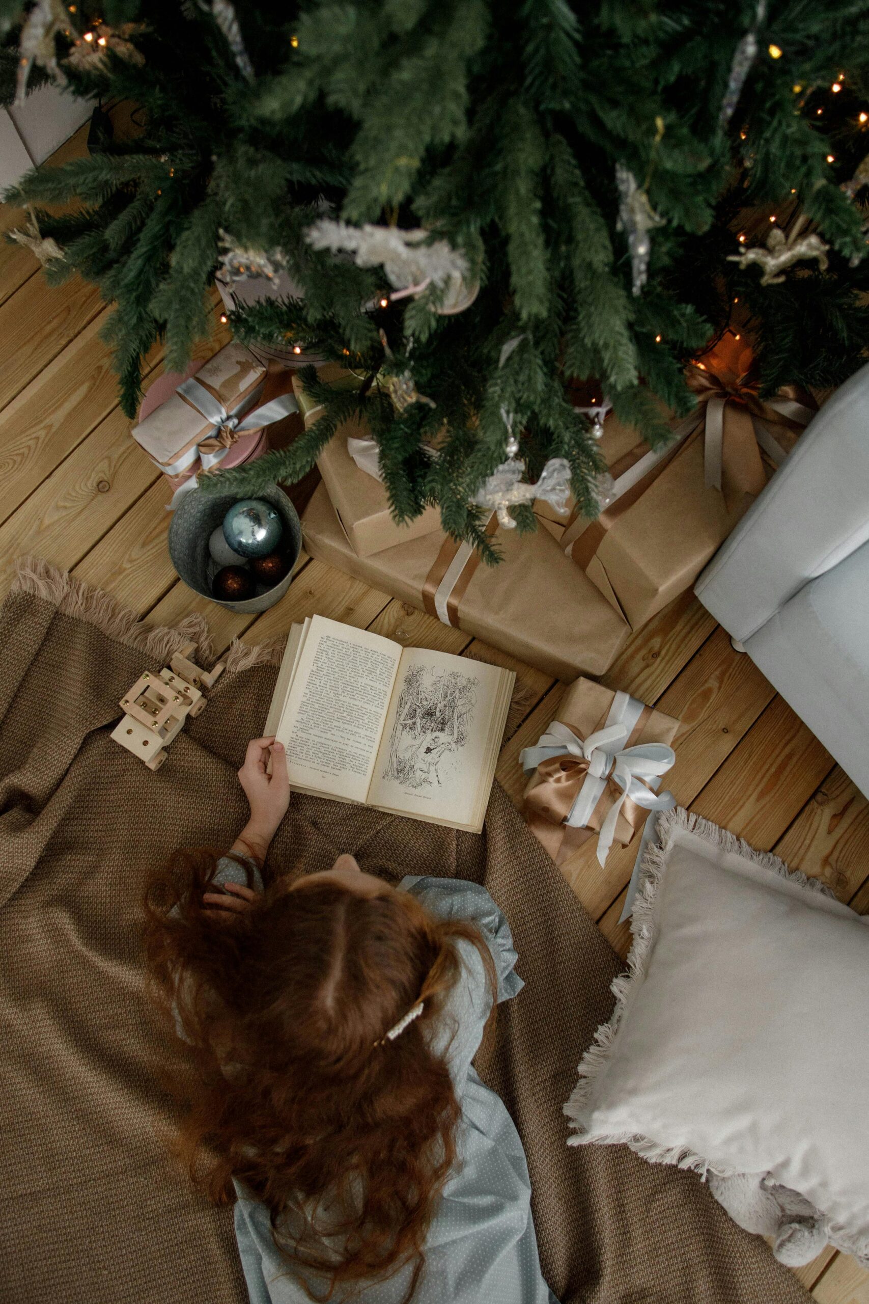 hild resting and reading under a Christmas tree during holiday overwhelm, a scene often associated with autistic and PDA burnout.