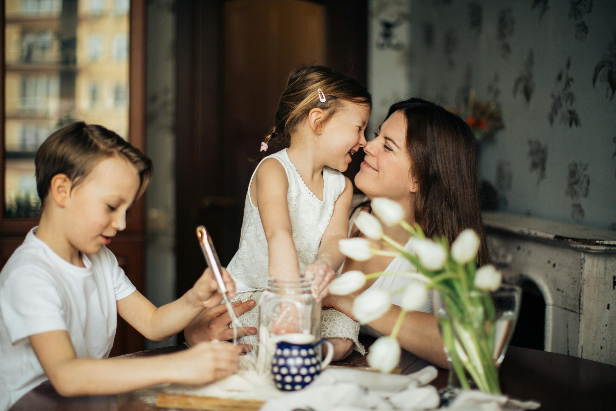 Mum having a nice moment with her daughter touches noses as they sit at the kitchen table.